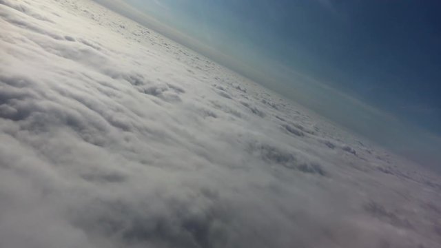 Above the clouds - filmed at a dutch angle from a passenger airliner. Daytime, blue sky, atmospheric, ethereal. Shifted horizon. Travel. Holiday. Heavenly. Stylised clouds, skyline.