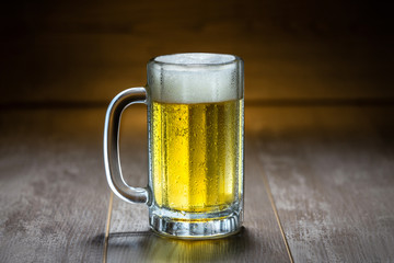 Classic cold refreshing bright lager pilsner beer in stein mug, on old wooden pub bar surface