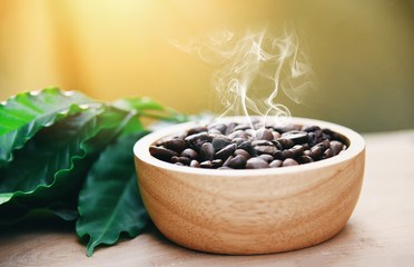 Roasted coffee beans on wooden bowl with green coffee leaf on wooden table