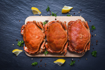 Cooked crabs on wooden board with lemon on plate served on dark plate top view - stone crab steamed seafood