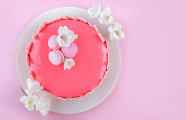 Pink mousse cake with mirror glaze decorated with macaroons, flowers for Happy Birthday on pink holiday background. Holiday cake celebration. Top view, flat lay