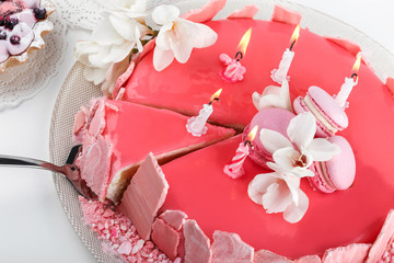 Pink mousse cake with mirror glaze decorated with macaroons, flowers for Happy Birthday on pink holiday background. Holiday cake celebration, close up
