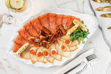 Seafood platter with salmon slice, smoke sturgeon, quail eggs with red caviar, slices fish fillet, decorated with arugula and lemon on marble background. Mediterranean appetizers, closeup, macro
