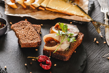 Sandwich with smoked mackerel fish with spices on dark stone background. Smoked fish, mediterranean...