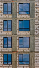 Wall of modern apartment building with just-mounted windows with sky reflection