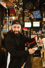 smiling barman pouring beer in a bar. Bearded courageous man pours you a foaming drink.