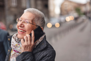 Happy senior old woman talking on her cell phone in the street