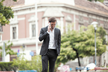 Cheerful happy young business man enjoying a nice talk over his phone, walking the streets of a city