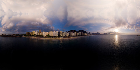 Fototapeta na wymiar Aerial 360 degree panorama of Copacabana beach in Rio de Janeiro with dramatic blue sky with clouds and play of light at sunrise seen from the ocean ready for use in 3D environment mapping and 360VR