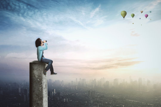 Afro student looks at air balloons with binoculars