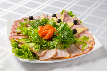banquet cutting with ham, meat delicacies, cheese, sausage smoked, olive, lettuce and tomato on white dish