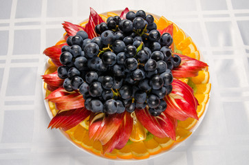 sliced fruit - apples, oranges, kiwi topped with grapes on white dish