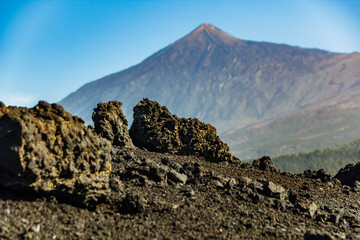 Big lava rock in focuse at the center of photo and mountain Teide , partly covered by the clouds on...