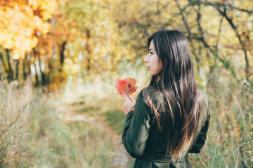 Naklejka premium Female beauty portrait surrounded by vivid foliage. Dreamy beautiful girl with long natural black hair on autumn background with colorful leaves in bokeh. Fallen leaves in girl hands in autumn forest.