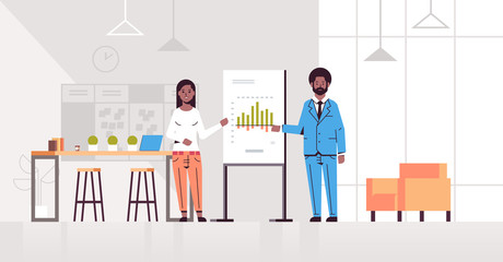 coworkers presenting financial graph on flip chart african american business couple at conference meeting making presentation concept modern office interior flat full length horizontal