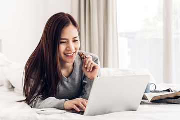 Young woman relaxing and drinking cup of hot coffee or tea using laptop computer on a cold winter day in the bedroom.woman checking social apps and working.Communication and technology concept