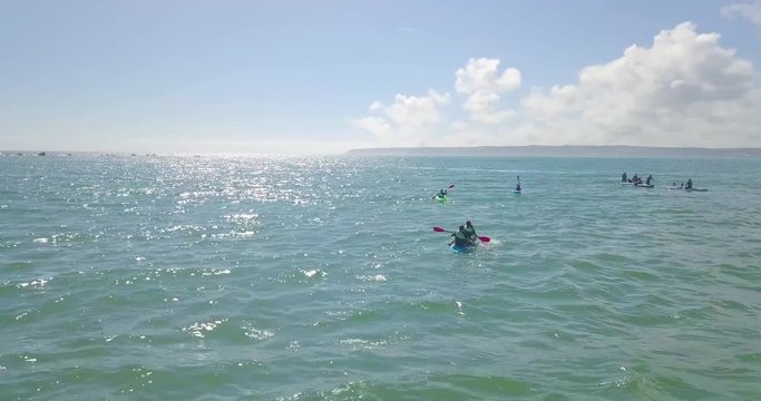 Group of people and tourists kayaking out into the ocean in cornwall in the summer from a drone aerial view