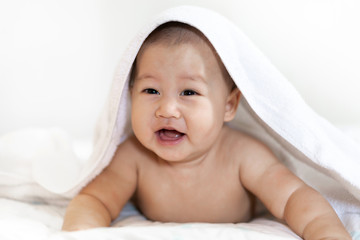 Portrait of happy smile baby relaxing under towel after bath on the bed