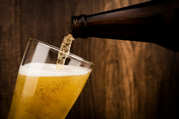 Pouring cool beer from bottle into glass on wood wall backgroud alcohol celebration concept