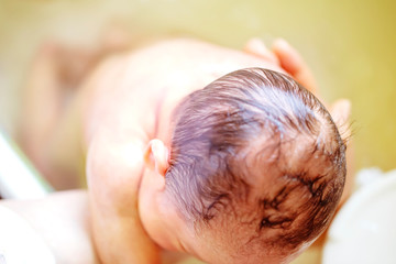 薬草の煎じ汁を入れたお風呂に浸かる生後2週間の赤ちゃんの背中を洗う