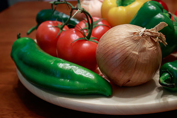 red tomatoes, peppers, and golden onions around on a table in a kitchen