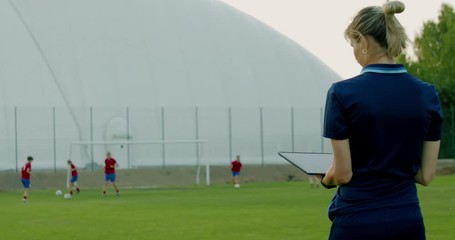 Female coach using tablet during teenager girl soccer football team practice. 4K UHD 60 FPS SLOW MOTION
