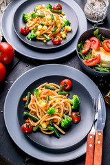 Pasta with vegetables and salad with arugula and mozzarella on a dark wooden background. Traditional Mediterranean cuisine. Vertical shot