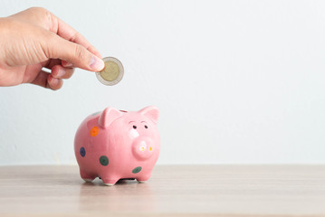 Woman hand putting coin to pink piggy bank with copy space for text