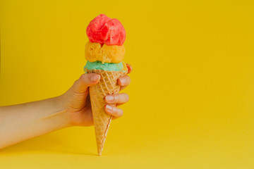 female hand holding waffle cone ice cream isolated on a vibrant yellow background, copy space