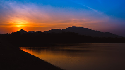 Sunset landscape with orange sky, silhouettes of mountains, hills and trees and lake