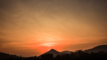 Sunset landscape with orange sky, silhouettes of mountains, hills and trees and lake