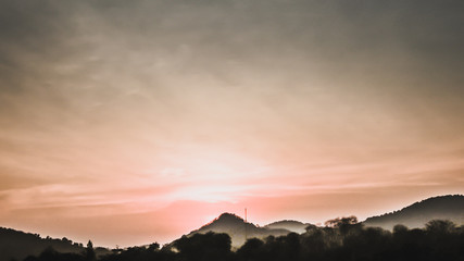 Obraz premium Sunset landscape with orange sky, silhouettes of mountains, hills and trees and lake