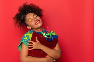 dark-skinned and curly girl with colored bags for shopping in stores. waiting for new purchases. girl on red Studio background