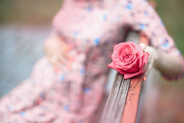 Pregnant woman touching bump whilst holding pink rose girl waiting