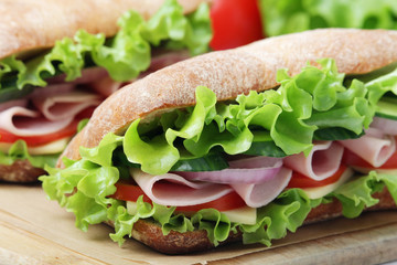 Two sandwiches with fresh vegetables, ham and cheese in ciabatta bread