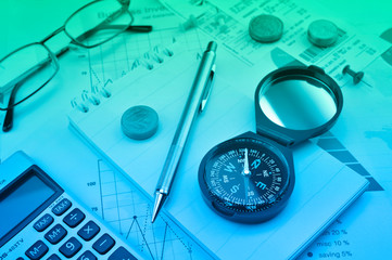 Blue compass, pen, coin, notebook, calculator, glasses on financial graph, Business investment concept