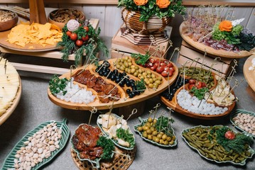 Antipasti board with various cheese and meat snacks with hummus and olives on wooden round board on black table