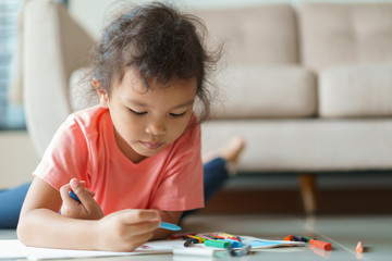 Cute little asian girl drawing homework and writing with color Wax crayons on paper in her home
