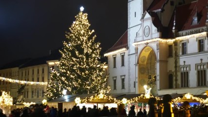 Christmas tree luminous and shines beautiful decorated with golden ornaments and flasks, historical architectural city, market and goods stalls