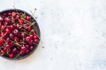 Red ripe sweet cherry berries in bowl with sticks on light white background. Top above view.