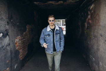 Portrait of young man in blue jeans jacket with sunglasses outdoor on dark background.