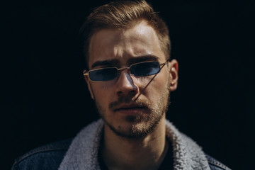 Portrait of young man in blue jeans jacket with sunglasses outdoor on dark background.