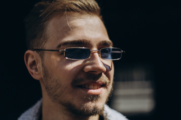 Portrait of young man in blue jeans jacket with sunglasses outdoor on dark background.