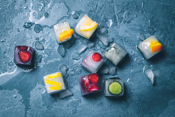 Ice cubes with fruit and broken ice on a stone blue background. Mint, strawberry, cherry, lemon, orange. Flatlay, top view