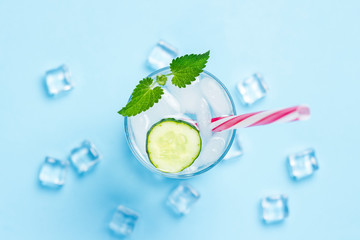 Glass of cold and refreshing water with ice, mint and cucumber on a blue background. Ice Cube. Concept of hot summer, alcohol, cooling drink, thirst quenching, bar. Flat lay, top view