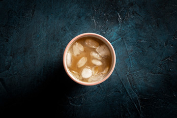 Coffee with ice and milk in a glass on a dark blue stone background. Concept cooling drink, thirst, summer, ice, nightlife, club. Flat lay, top view