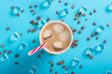 Refreshing coffee with milk and ice in a glass, ice cubes and coffee grains on a blue background. Concept summer, ice, refreshing cocktail, thirst. Flat lay, top view