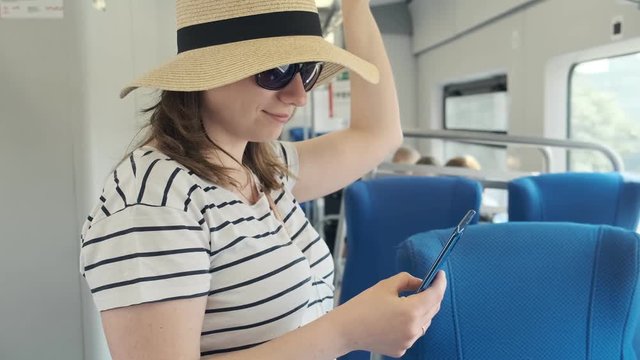 Young woman using smart phone in train. Portrait of cute girl in hat holds handrail and typing message on her phone. Medium shot with copyspace