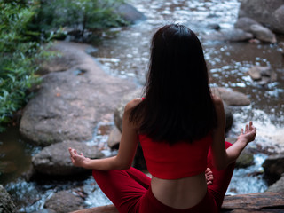 Asian woman practicing or doing yoga at the waterfall. Beautiful Landscape, Natural background, Thailand. Rear view