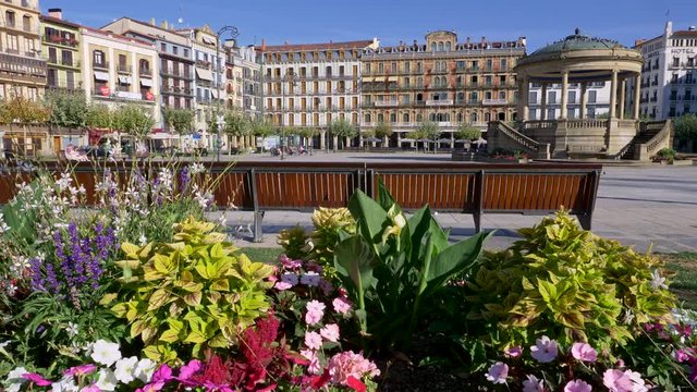 Pamplona, Spain. Bright colored flowers by a bench on a Plaza del Castillo. Lifting shot over flowers to get a wide view of the place. 4K